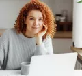 White woman with red curly hair on her laptop